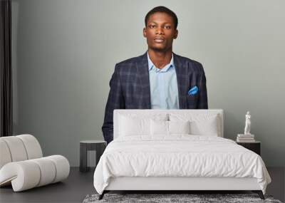 Handsome African American businessman stands confidently with hands in pockets wearing checkered blazer on grey backdrop. Wall mural