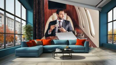 handsome businessman in suit holding cup of coffee in private plane Wall mural