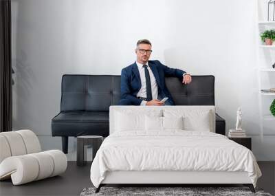 handsome businessman in suit sitting on sofa and holding smartphone Wall mural