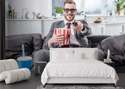 handsome businessman on couch in 3d glasses with remote control watching movie and eating popcorn Wall mural