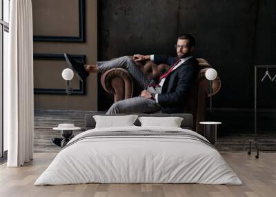 handsome elegant businessman posing in armchair, hat lying on floor near, loft interior Wall mural