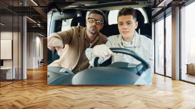 handsome father pointing on something while teaching teen son driving car Wall mural