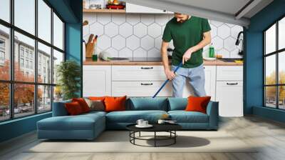 handsome joyous man in comfortable casual attire using mop to clean floor while in kitchen at home Wall mural