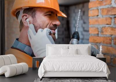 handsome man holding hammer drill and touching earphones Wall mural