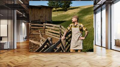 handsome man in casual attire with tattoos posing next to fence and manure on farm and looking away Wall mural