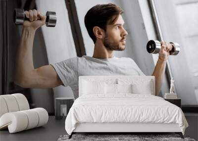 handsome young man exercising with dumbbells and looking at window at home Wall mural