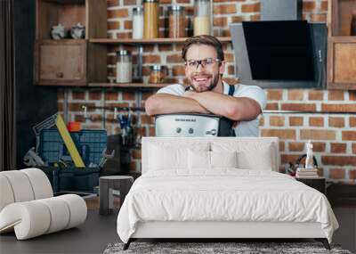 handsome young repairman leaning at coffee machine and smiling at camera Wall mural