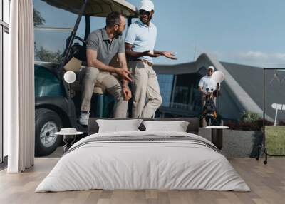 Happy adult multiethnic friends talking while sitting on golf cart Wall mural