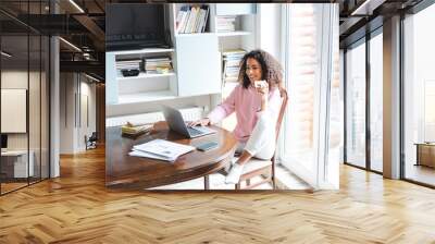 happy african american freelancer holding cup while using laptop at home Wall mural