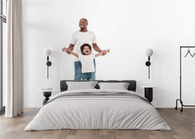 happy african american man supporting cheerful son standing on penny board on white background Wall mural