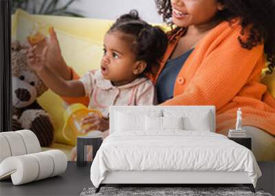 happy african american mother sitting near toddler daughter with baby bottle Wall mural