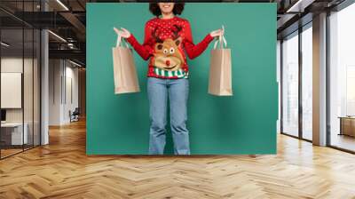 happy african american woman in sweater with deer and red horns headband levitating with shopping bags on green background Wall mural