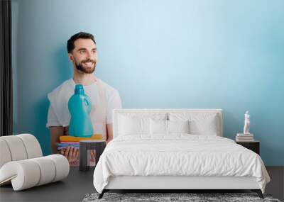 happy bearded man holding clean clothing and laundry detergent on blue Wall mural