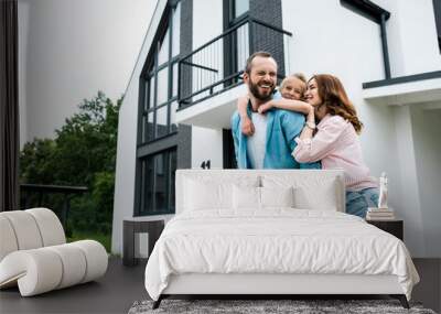 happy bearded man piggybacking daughter near cheerful wife and home Wall mural