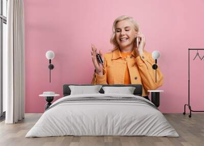 Happy blonde woman holding car key and talking on mobile phone isolated on pink Wall mural