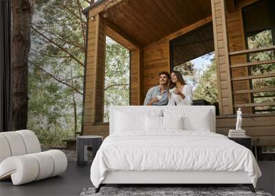 happy couple holding cups of coffee, man and woman smiling on porch of vacation house, hot beverage Wall mural