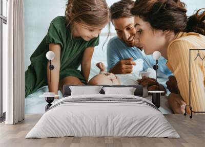 happy family looking at adorable infant lying on white bedding Wall mural