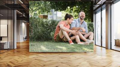 happy father laughing while sitting near teenage son on green lawn in park. Wall mural