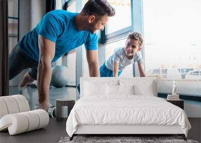 happy father looking at cheerful son and exercising with dumbbells Wall mural