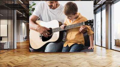 happy father teaching smiling son how to play acoustic guitar Wall mural