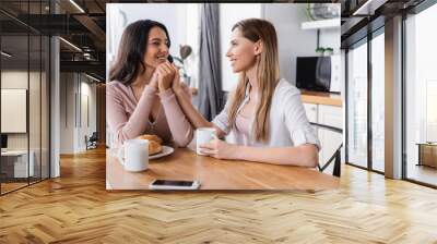 happy lesbian couple holding hands near breakfast and smartphone on kitchen table Wall mural