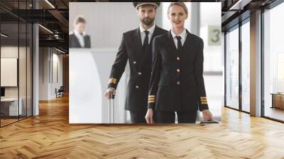 happy male and female pilots walking by airport lobby with suitcases Wall mural