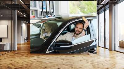 Happy man holding credit card while driving car at gas station Wall mural