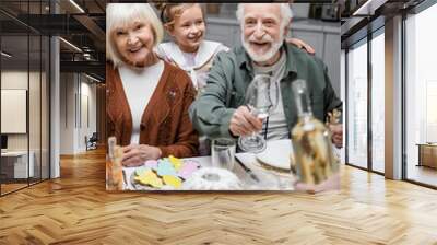 happy man holding glasses near bottle of wine during easter dinner with family. Wall mural