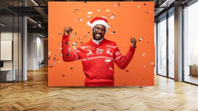 happy man in santa hat under falling confetti showing yes gesture on orange background Wall mural