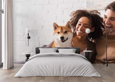 Happy man looking at smiling african american girlfriend with shiba inu at home, banner Wall mural