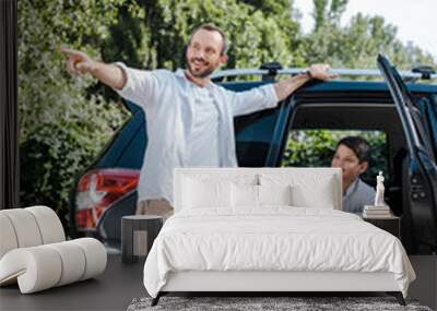 happy man standing and pointing with finger near son in car Wall mural