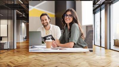 happy manager in eyeglasses smiling at camera near blurred colleague and paper cup on work desk. Wall mural