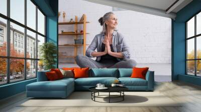 happy mature woman with grey hair sitting with praying hands in lotus pose on yoga mat Wall mural