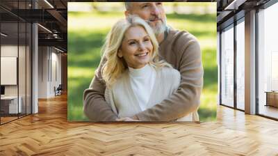 happy middle aged man with grey beard hugging charming wife in green park. Wall mural