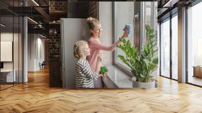 Happy mother and daughter cleaning window with rag and spray bottle together Wall mural