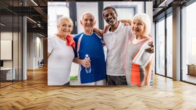 happy multicultural senior sportspeople looking at camera and embracing each other at gym Wall mural