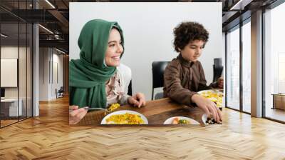 happy muslim girl in hijab eating pilaf near arabian brother. Wall mural