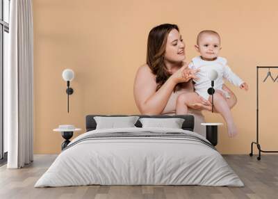 Happy plus size woman holding hand of child isolated on beige. Wall mural