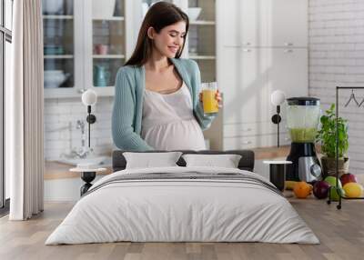 happy pregnant woman touching tummy while holding fresh juice in kitchen Wall mural