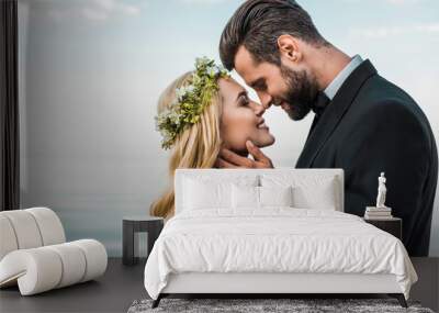 happy wedding couple in suit and white dress touching with noses on beach Wall mural