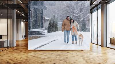 happy woman holding leash while walking together with boyfriend and akita inu dog under falling snow. Wall mural