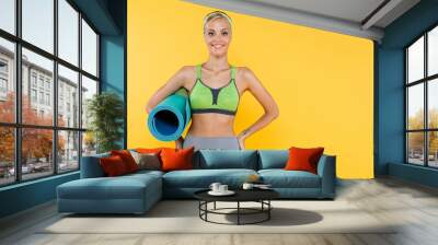 happy woman in sportswear standing with fitness mat and hands on hips isolated on yellow Wall mural