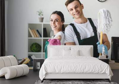 happy young cleaners with mop and spray bottle smiling at camera while cleaning office Wall mural