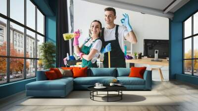 happy young cleaning company workers holding cleaning equipment and showing ok sign Wall mural