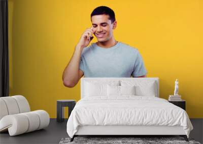 happy young man in t-shirt talking on mobile phone isolated on yellow. Wall mural