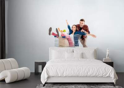 Happy young man pushing shopping cart with excited woman and grocery bag on white Wall mural