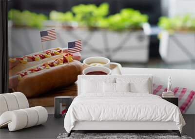 hot dogs with small us flags, bowls with mustard and ketchup near plaid napkin on table outdoors Wall mural