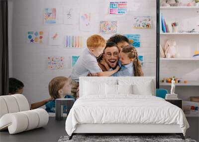 interracial kids hugging happy teacher at table in classroom Wall mural