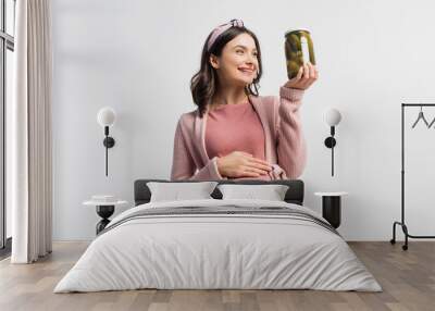 joyful pregnant woman in headband looking at jar with pickled cucumbers isolated on white Wall mural