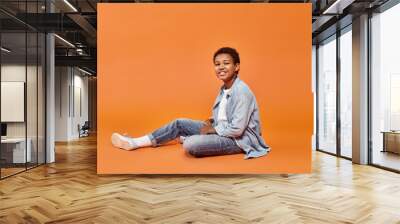 joyous african american boy in casual attire sitting on floor and smiling cheerfully at camera Wall mural